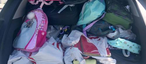 Car trunk filled with many backpacks and school supplies.